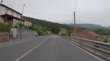 POV, güneşli bir günde Asturias köyünün evlerinden geçen boş bir yolda araba sürüyor. İspanya 'da küçük bir kasaba manzarası. Trafik yolları ulaşım kavramı.