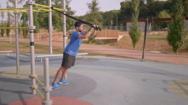 Sportsman working out with TRX system outside. Total body resistance exercises in city park. A handsome man is working out in street gym. Bodybuilder has fitness workout