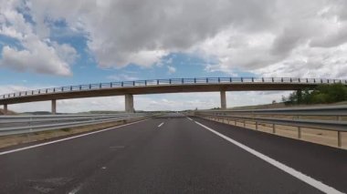 POV driving a car on empty highway road through the fields outside the city during sunny day. Two way asphalt road country views with low clouds at Spain. Traffic ways transportation concept.