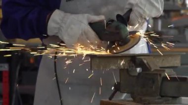 Slowmotion of a man welder with safety clothes polishes the metal angle grinder in the workshop, sideways flashes. Male hands in gloves cut a piece of iron with sparks fly in different directions.