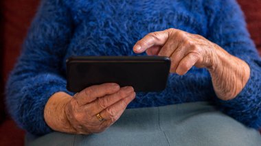 Yaşlı kadının buruşuk elleri akıllı telefon tutuyor. Yeni uygulama ya da web sitesi için telefon kullanan Kafkasyalı büyükannenin yaşlı ellerini kapat.