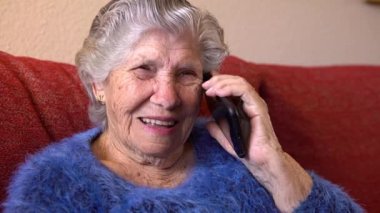 Mutlu gülümseyen büyükanne cep telefonundan konuşuyor. Yaşlı büyükanne telefon konuşması yapıyor. Kanepede otururken akıllı telefon kullanan yaşlı bir kadın. Teknoloji aygıtı kavramı