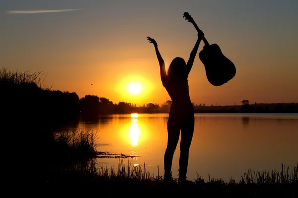 Silhouette eines glücklichen Mädchens mit einer Gitarre am Fluss — Stockfoto