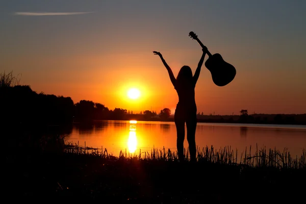 Silhueta de uma menina feliz com uma guitarra em um pôr do sol — Fotografia de Stock