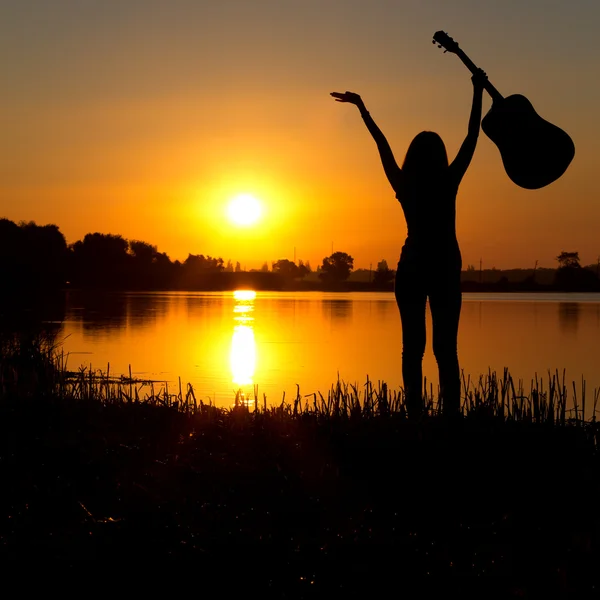 Silhouet van een gelukkig meisje met een gitaar op een zonsopgang — Stockfoto