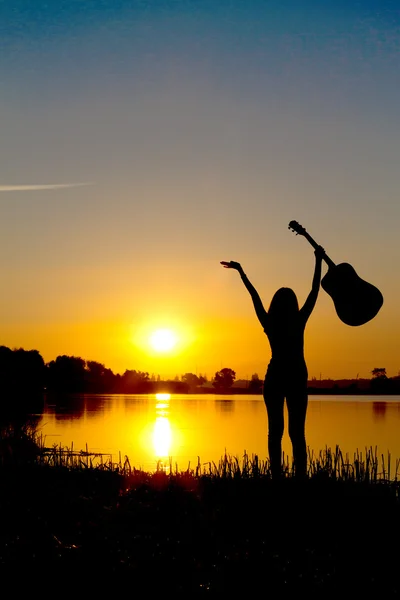 Silhouette eines glücklichen Mädchens mit einer Gitarre bei Sonnenaufgang — Stockfoto