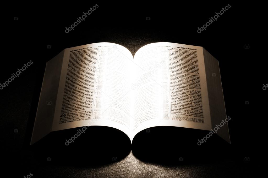 Open old Bible on a table with light shed on it