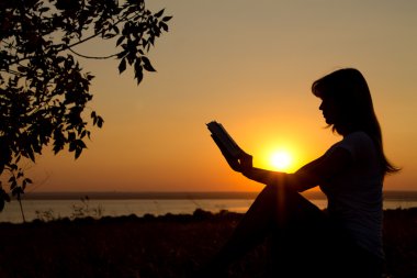 bir kız gün batımında elinde bir kitapla silüeti