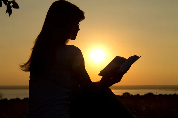 Silhueta de uma menina lendo ao pôr do sol — Fotografia de Stock