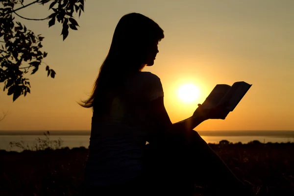 Silhouette of a girl reading at sunset — Stock Photo, Image