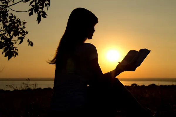 Silhueta de uma menina lendo ao pôr do sol — Fotografia de Stock