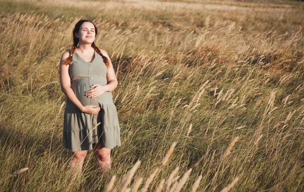 年轻美丽的孕妇在日落时分漫步在干枯蓬松的草丛中 在夏日的自然中悠闲自在 为分娩做准备 快乐健康的母亲 — 图库照片