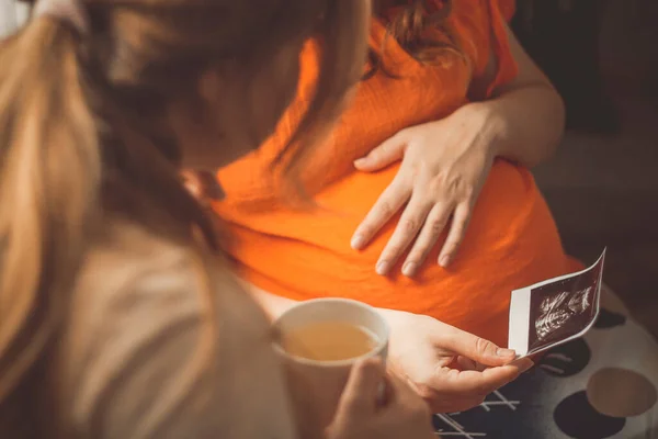 与姐姐坐在厨房里谈论超声波快照 母性观念 怀孕和友谊观念的年轻孕妇 — 图库照片