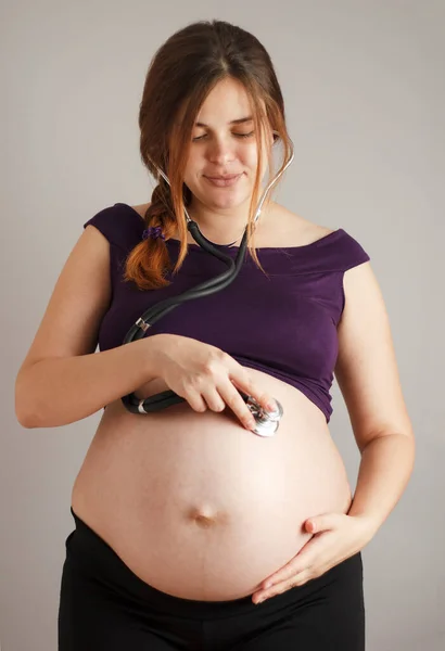 Schöne Rothaarige Schwangere Frau Die Mit Einem Stethoskop Ihrem Bauch lizenzfreie Stockfotos