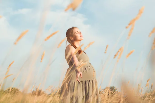 若い美しい妊婦は夏の自然乾燥したふわふわの草の間を歩く出産の準備幸せな健康な母親 リラックスした演習 — ストック写真