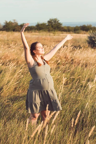 若い美しい妊婦は夏の自然乾燥したふわふわの草の間を歩く出産の準備幸せな健康な母親 リラックスした演習 — ストック写真