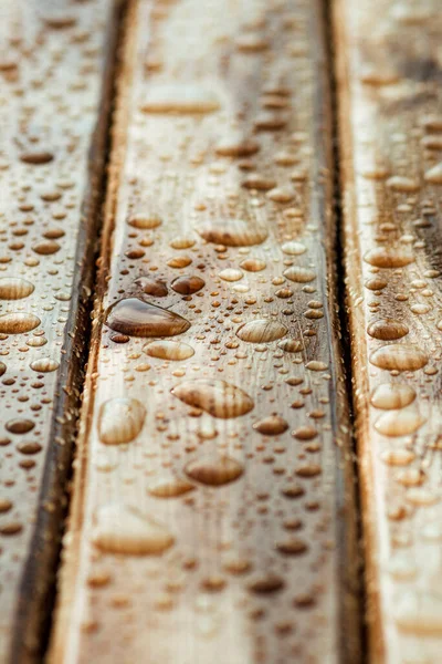 Yağmurdan yağan parlak su damlaları ve ıslak ahşap kalaslarla kaplanmış ahşap kaplama.