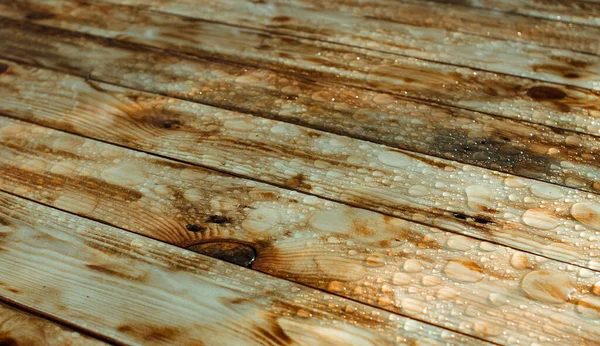 Yağmurdan yağan parlak su damlaları ve ıslak ahşap kalaslarla kaplanmış ahşap kaplama.