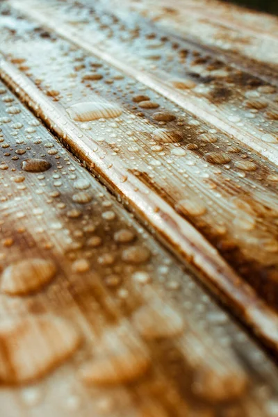 Yağmurdan yağan parlak su damlaları ve ıslak ahşap kalaslarla kaplanmış ahşap kaplama.