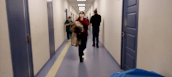 Teknolojik alanın, tıp ve hastane koridorunun, modern bir hastanenin odağından çıkmış soyut, bulanık arkaplanı. İnsanlar kapıya doğru yürür ve doktoru bekler..