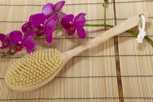 Bath brush on a mat of bamboo and an orchid