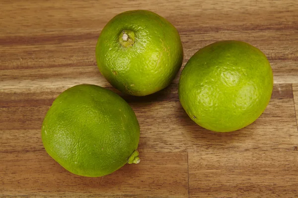 Three limes on a tabletop of acacia wood — Stock Photo, Image