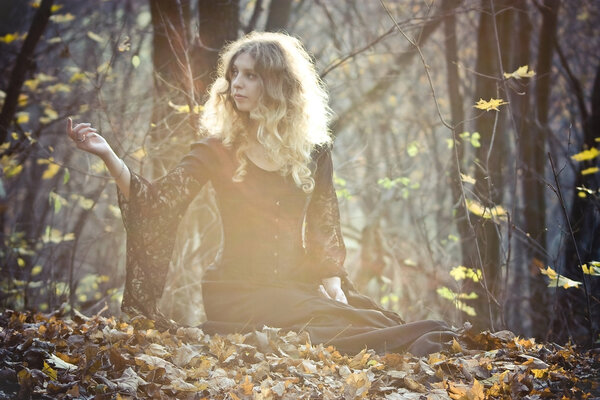 Young woman with her reised hand sits on the leaf in the fairy wood. Sunshine and haze.