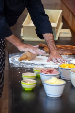 Önlükteki insan elinin yakın çekimi hamuru siyah ahşap bir masaya yoğur, un serp. Fırında elle para kazan..