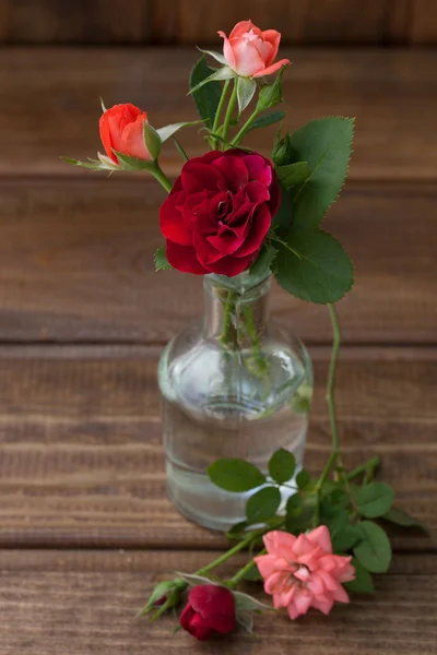 Pequeños brotes de rosas en una botella de vidrio sobre una textura de madera —  Fotos de Stock