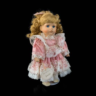 Siyah arka planda izole edilmiş porselen bebek. Seramik, eski pembe elbiseli yaşlı bir bebek.