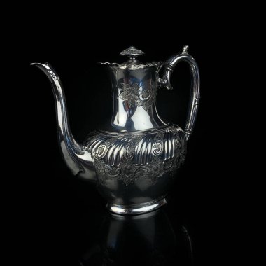 antique metal teapot. silver tea service. metal jug with engraving on a black isolated background. coffee pot