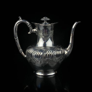 antique metal teapot. silver tea service. metal jug with engraving on a black isolated background. coffee pot