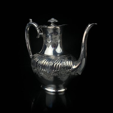 antique metal teapot. silver tea service. metal jug with engraving on a black isolated background. coffee pot