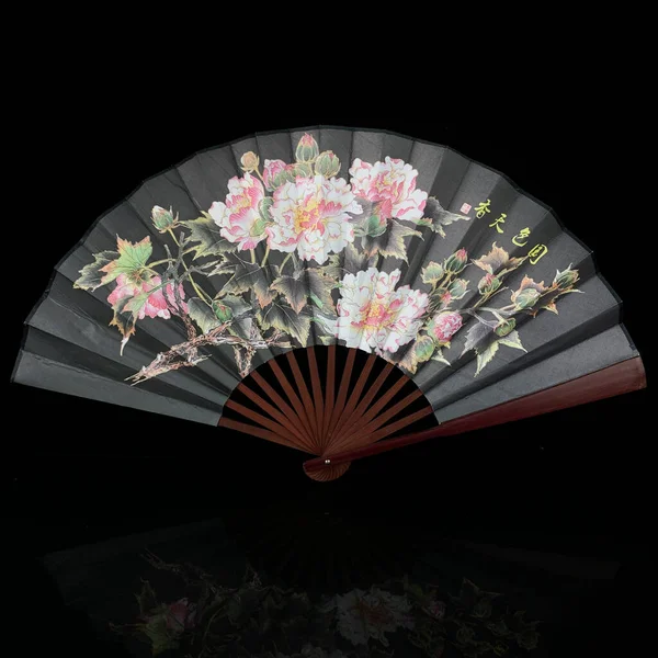antique gray fan with painted flowers on a black isolated background. fan with Chinese painting close-up. flower fan