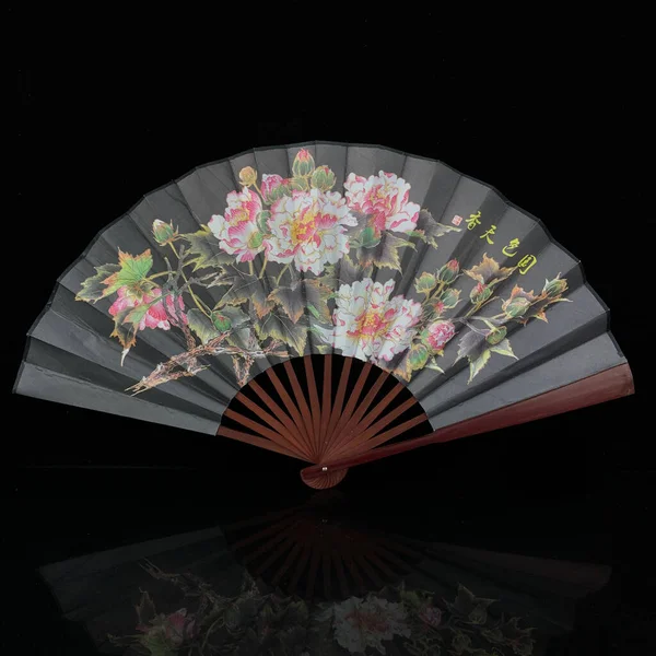 antique gray fan with painted flowers on a black isolated background. fan with Chinese painting close-up. flower fan
