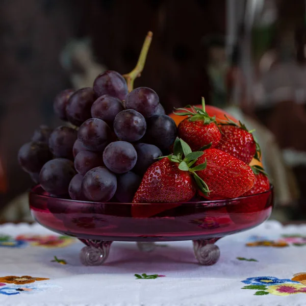 Fresh strawberries and grapes in a crystal bowl. Bright summer still life with fruits