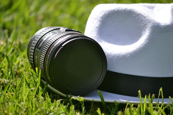 Lente da câmera e chapéu branco na grama — Fotografia de Stock