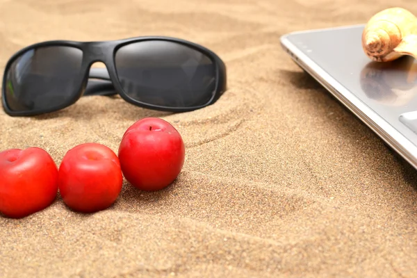 Ciruelas, gafas de sol y ordenador sobre arena —  Fotos de Stock