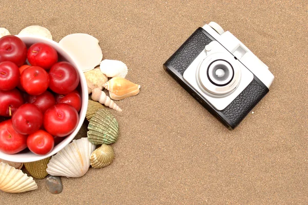 Prunes rouges, vieil appareil photo, coquilles et chapeau blanc sur sable — Photo