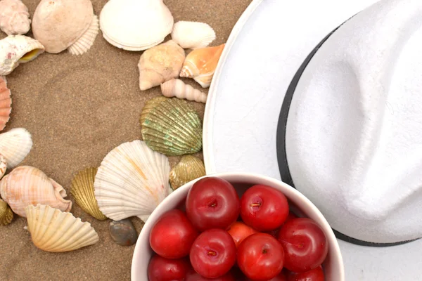 Śliwki czerwone, muszle i biały kapelusz na piasku — Zdjęcie stockowe