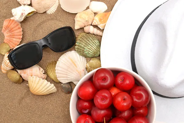 Sunglasses,shells,plums and white hat on sand — Stock Photo, Image