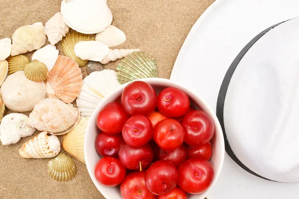 Red plums, shells and white hat on sand — Stock Photo, Image