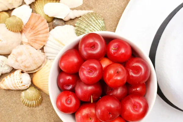 Red plums, shells and white hat on sand — Stock Photo, Image