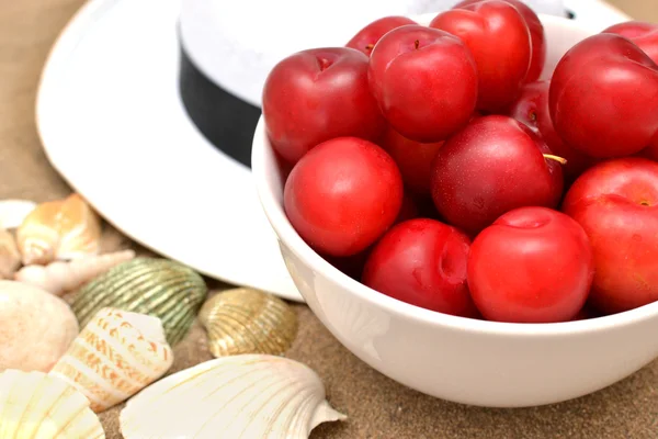 Prunes rouges, coquillages et chapeau blanc sur sable — Photo