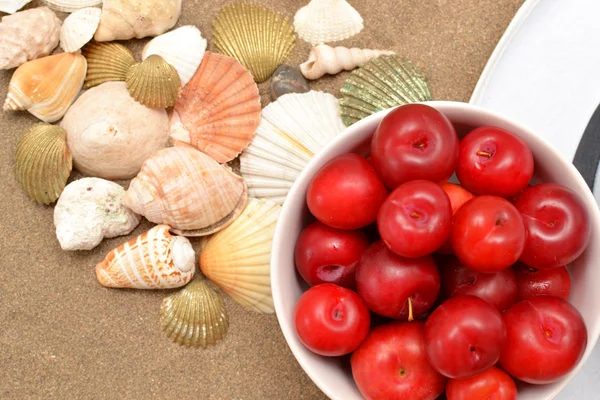 Red plums, shells and white hat on sand — Stock Photo, Image