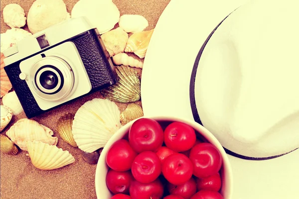 Prunes rouges, vieil appareil photo, coquillages et chapeau blanc sur sable vintage — Photo
