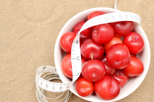 Red plums and tape measure — Stock Photo, Image
