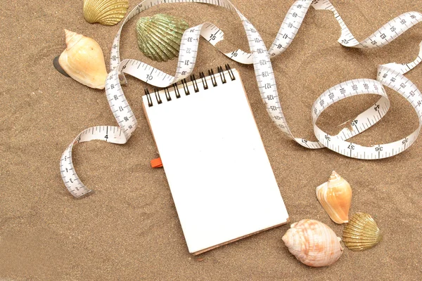 Notebook and tape measure on sand — Stock Photo, Image