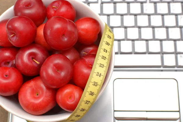 Red plums, laptop and tape measure on sand — Stock Photo, Image