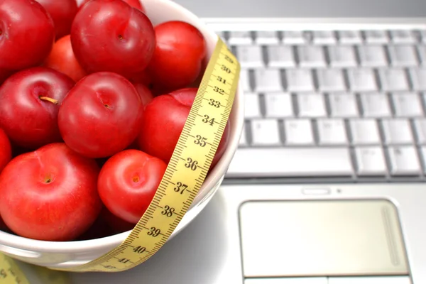 Red plums, laptop and tape measure on sand — Stock Photo, Image
